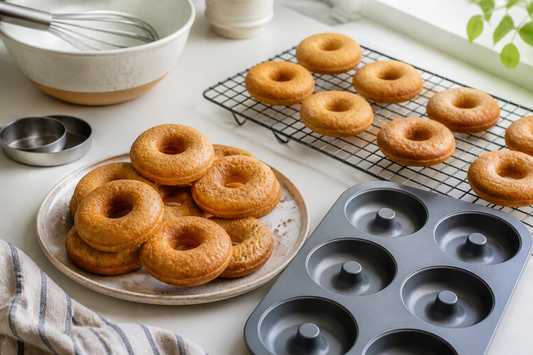 Freshly baked cake donuts beside a six-cavity donut mold and cooling rack